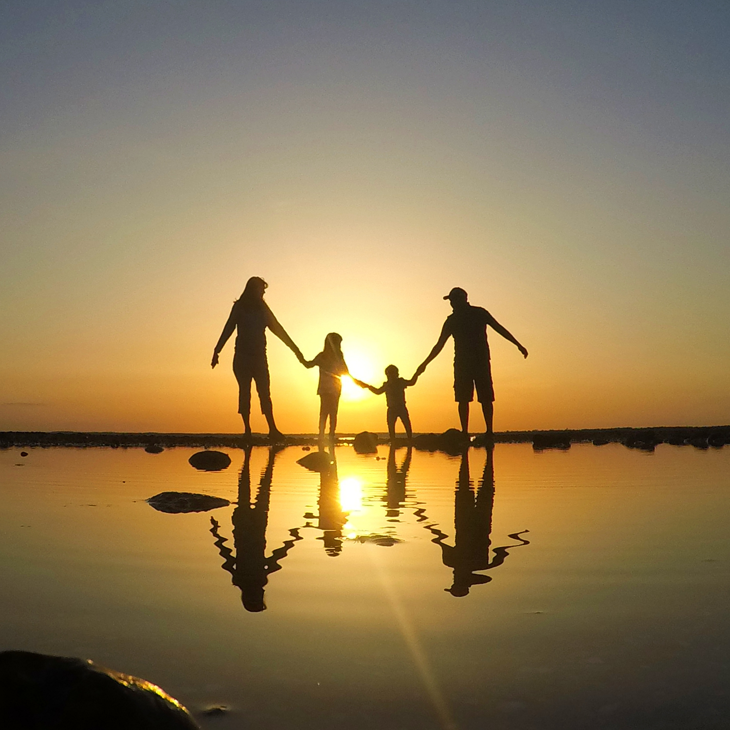 Family of 4 holding hands on the beach at sunset